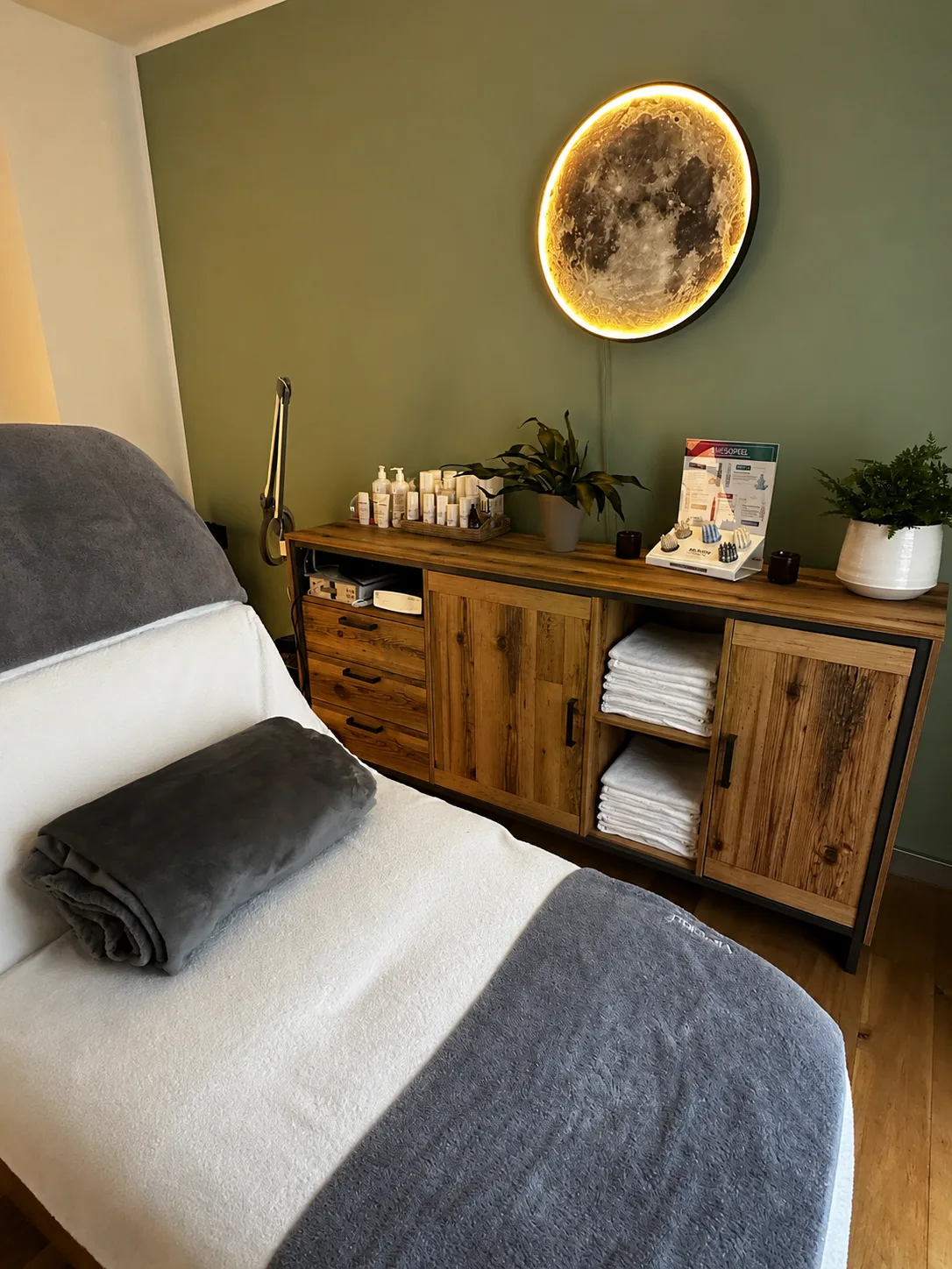 Behandlungsraum mit frischen Handtüchern, salbeigrüner Wand und leuchtender Mondlampe im Kosmetikstudio Beauty Concept Munich in München Au-Haidhausen